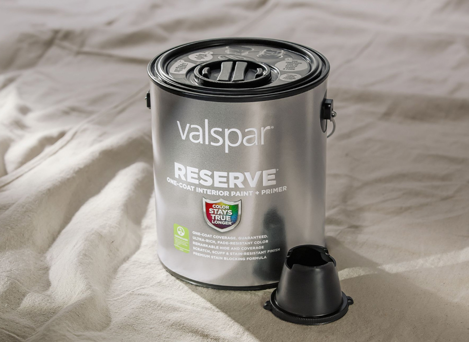 Gloved hand with brush applying stain to wood railing.