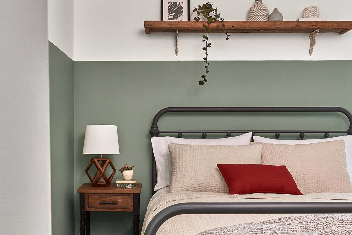 Bedroom wall painted moss green halfway up the wall to a light neutral. Rustic bed with layers of textured coverings.