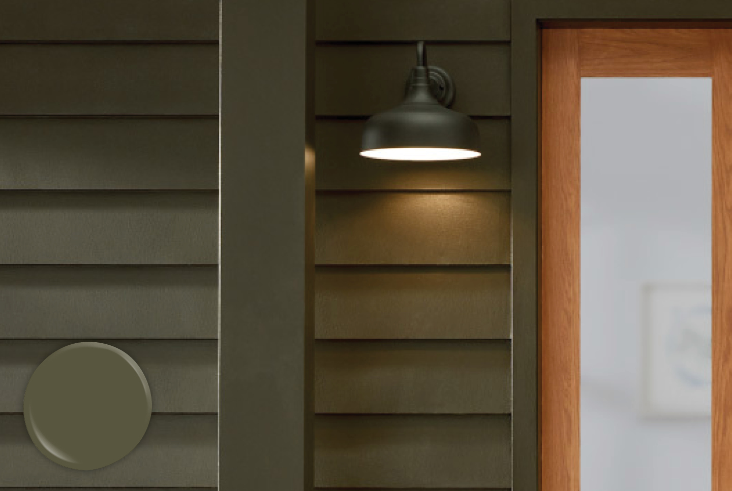 Olive Green siding illuminated by an outdoor light fixture and light wood entry door.