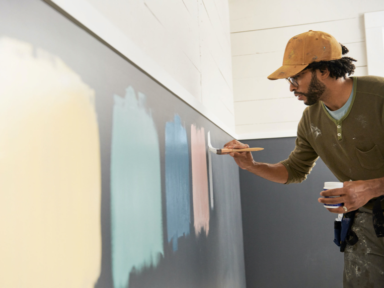 Painter holding sample size paint can painting large swatches of colors on wall.