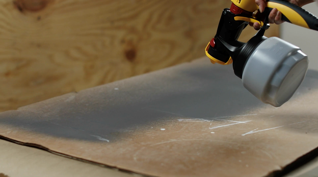 Sprayer spraying gray paint on scrap cardboard.