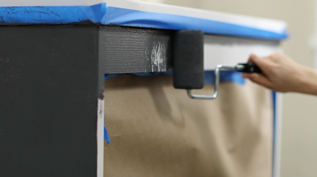 Prepped cabinet with blue painter’s tape. Small roller applying black paint.