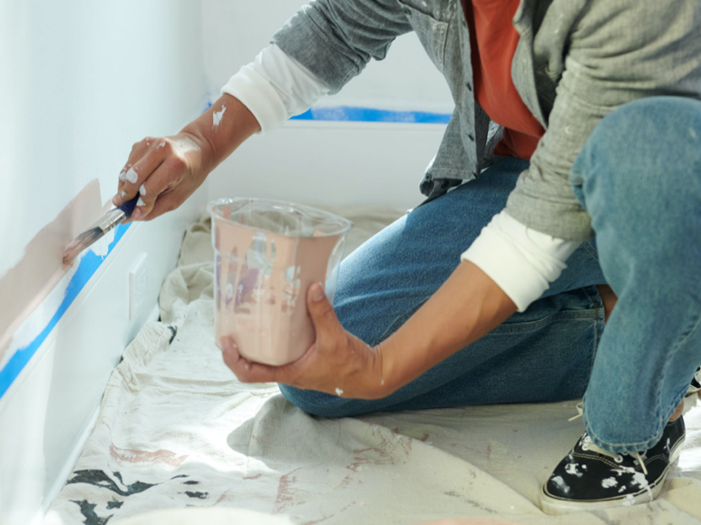 Person using a brush to apply a muted tan color to lower wall.